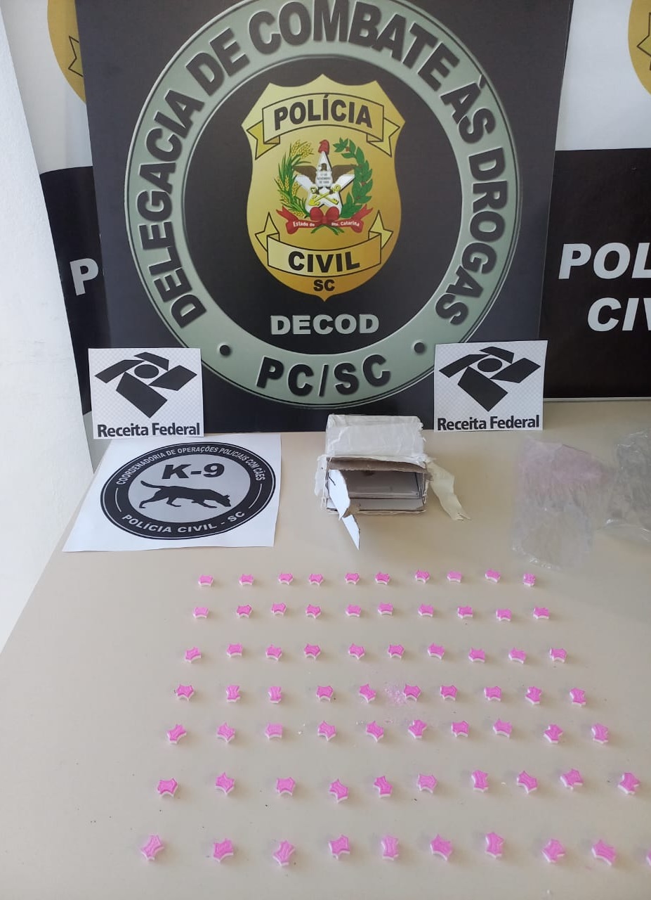 BANNer da Polícia Civil da Delegacia de Combate às Drogas, dois emblemas da Receita Federal, um emblema da Coordenadoraria de Operações Policiais com cães e comprimidos de ecstasy
