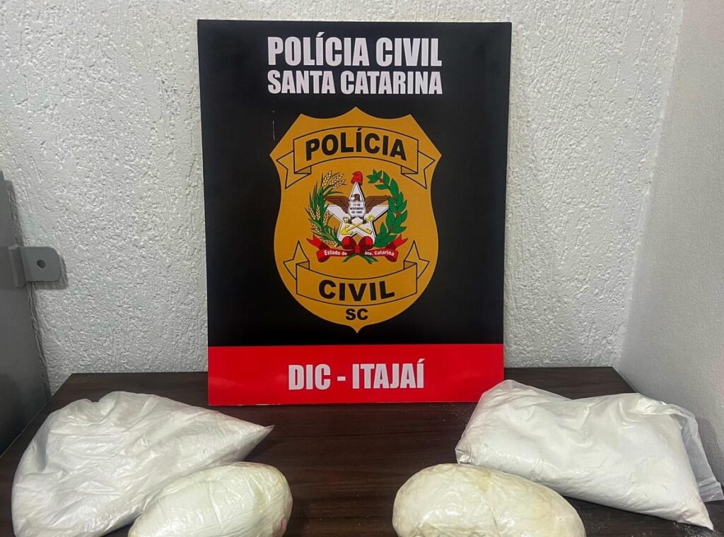 banner da DIC Itajaí e na mesa quatro sacos de cocaína
