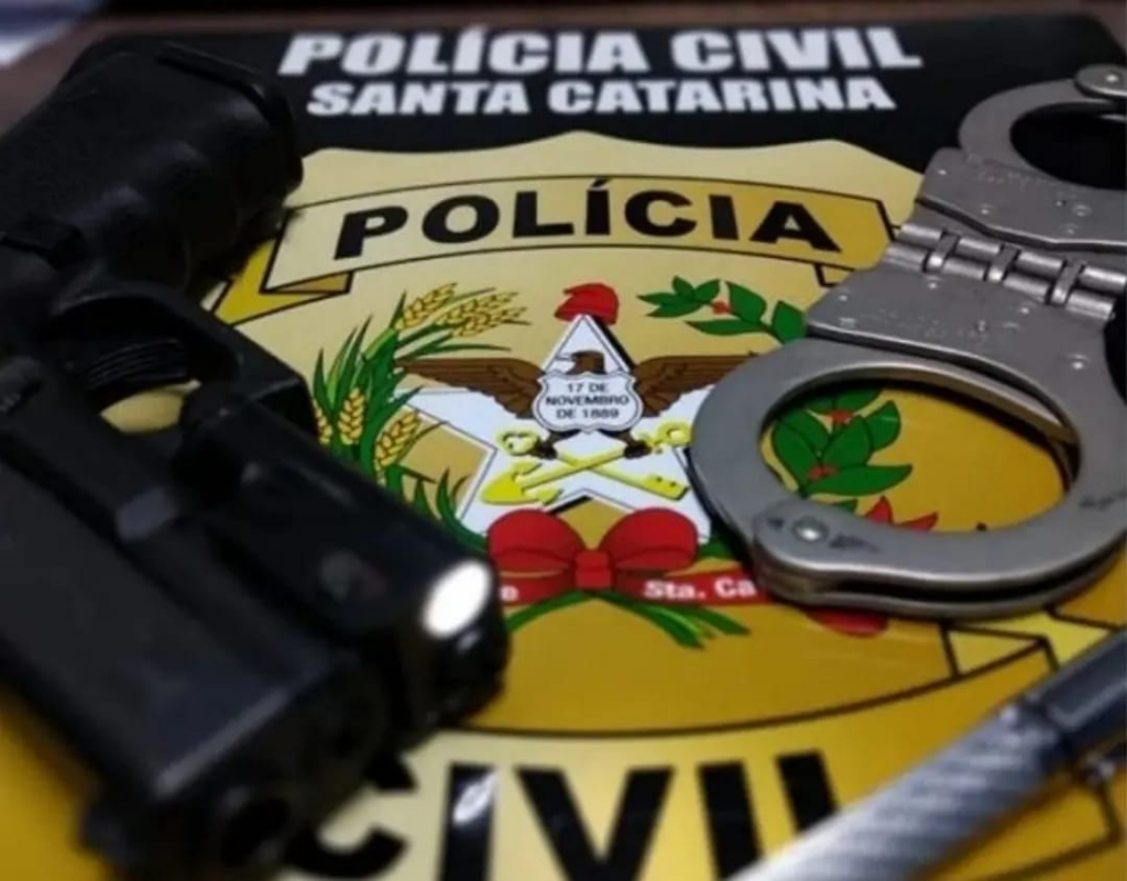 arma e algemas sobre uma mesa com a logo policia civil de sc