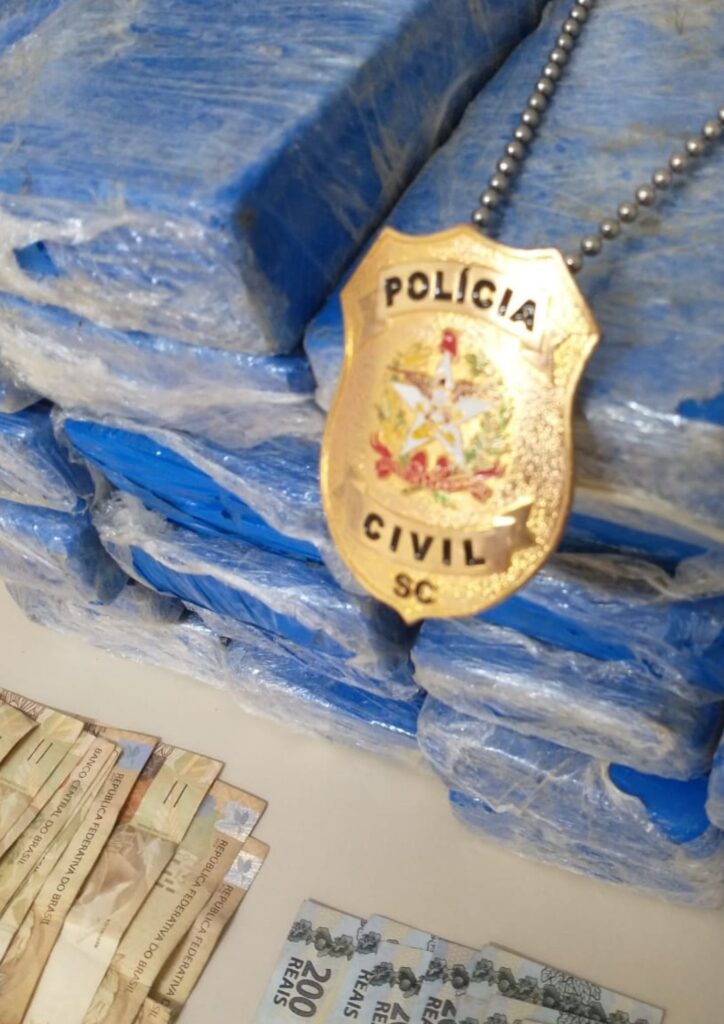 insignia da Policia Civil encima de tabletes de droga e dinheiro os mesmos sobre uma mesa com dinheiro