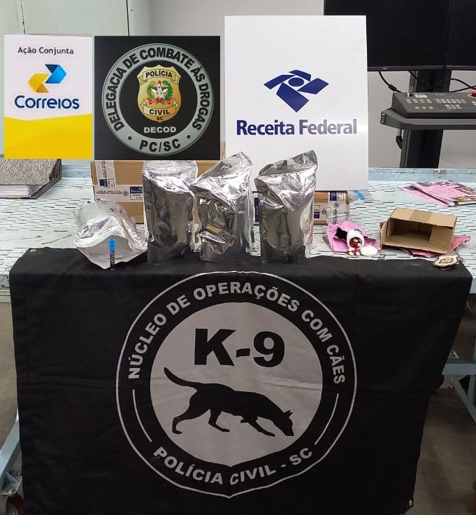 itens apreendidos encima de uma mesa, logo do K-9(operação de cães a policia civil), logo também da receita federal e do correios